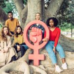 Group of people look defiantly at camera around large icon symbol of feminism