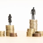 Gender Wage gap concept. Man and woman figurines standing on top of the pile of coins